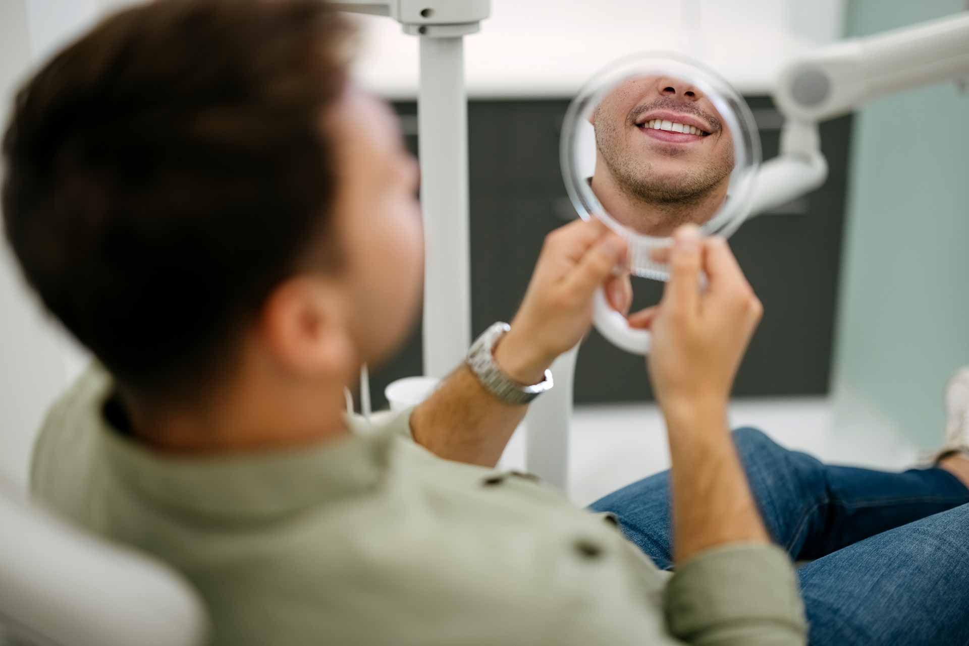 Satisfied man looks in the mirror and smiles after treatment at the dentist