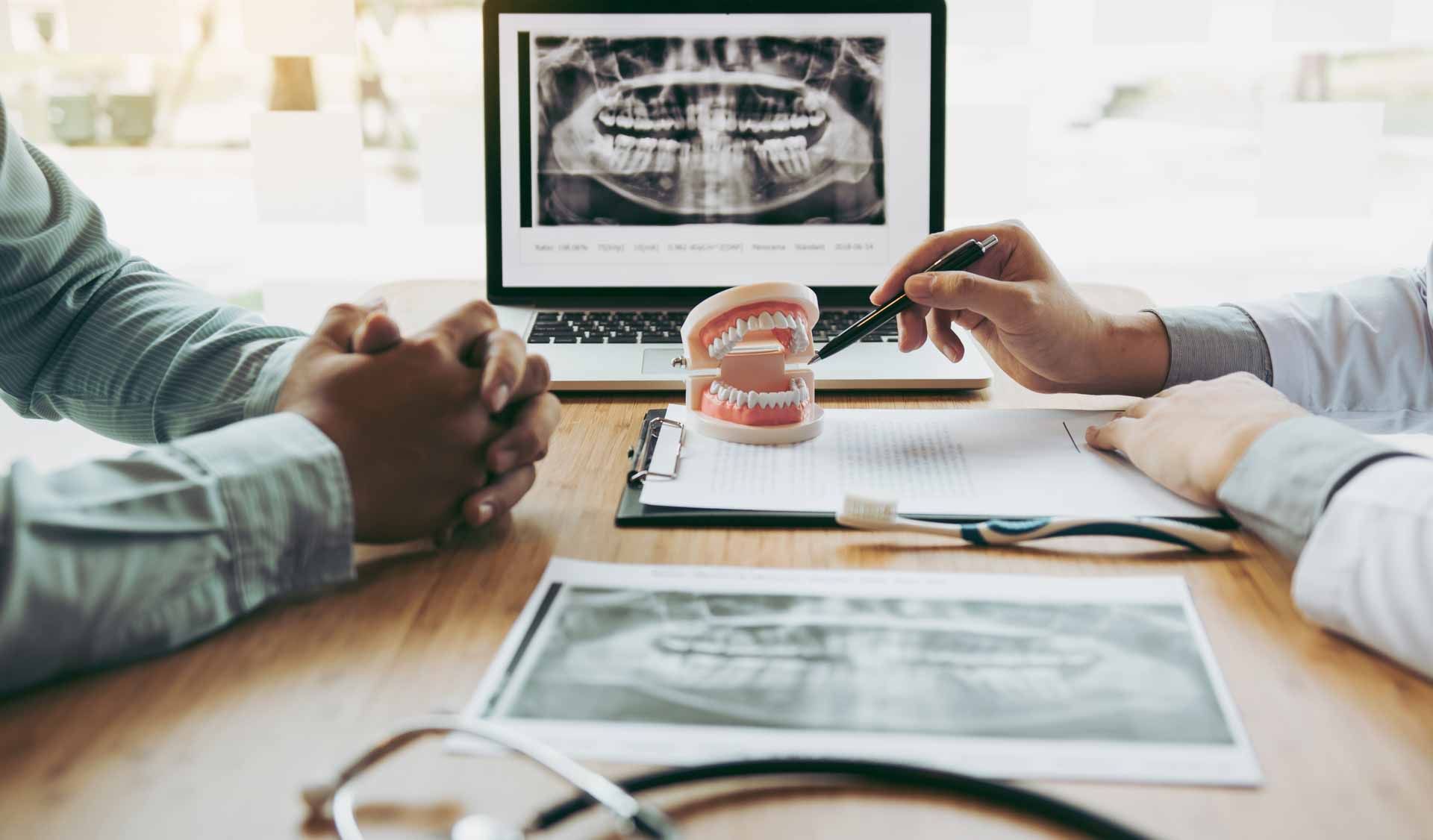 Dentist hand pointing x-ray picture in laptop computer and talking to the patient about medication and surgery treatment.